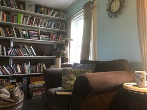 Image description: Dr. Andersen's favorite large brown chair with bookshelves and a coffee mug